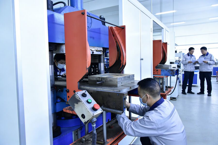 An operator loading a mould at a press, with the rest of the line behind.