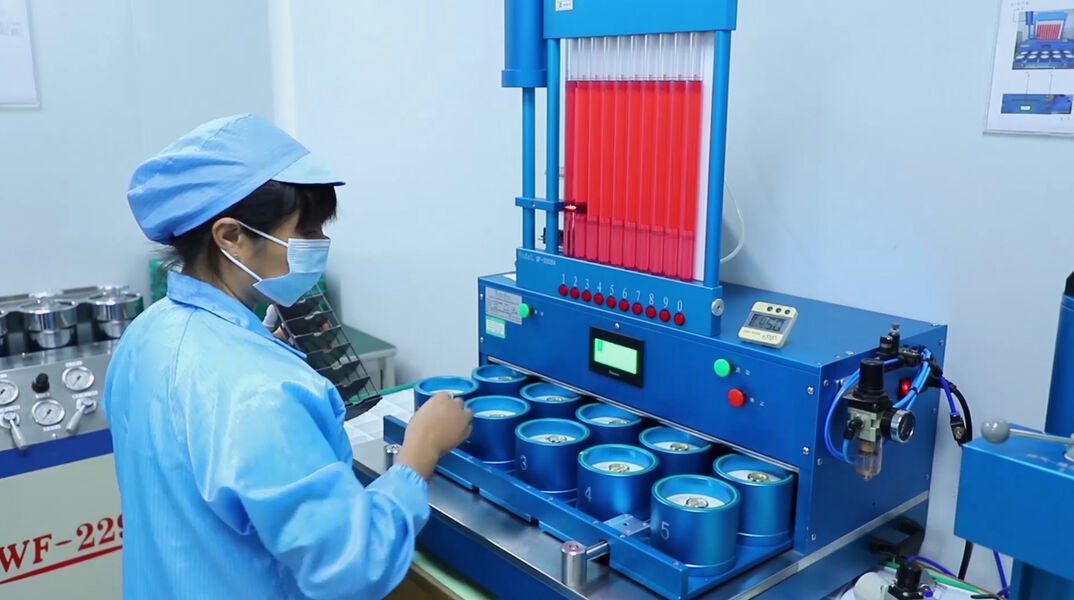 An operator in cap, coat and mask loading a ten station test rig. SHX runs tensile, buckle pull, fatigue, salt spray, abrasion and colour fastness tests in house.